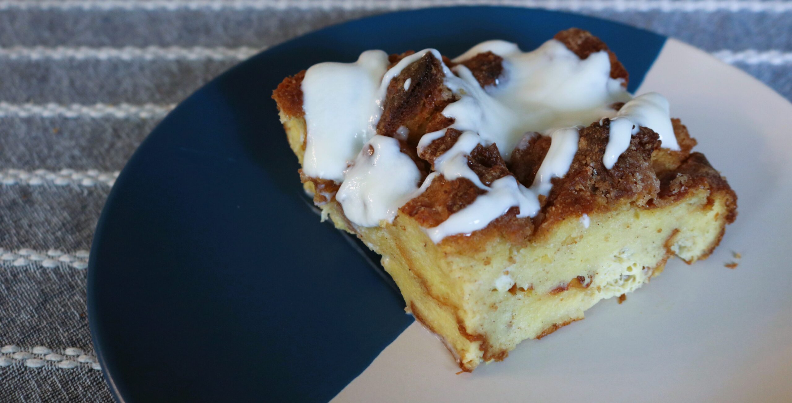 Slice of baked French toast sitting on a blue and white plate with stripes of maple yogurt over the top.