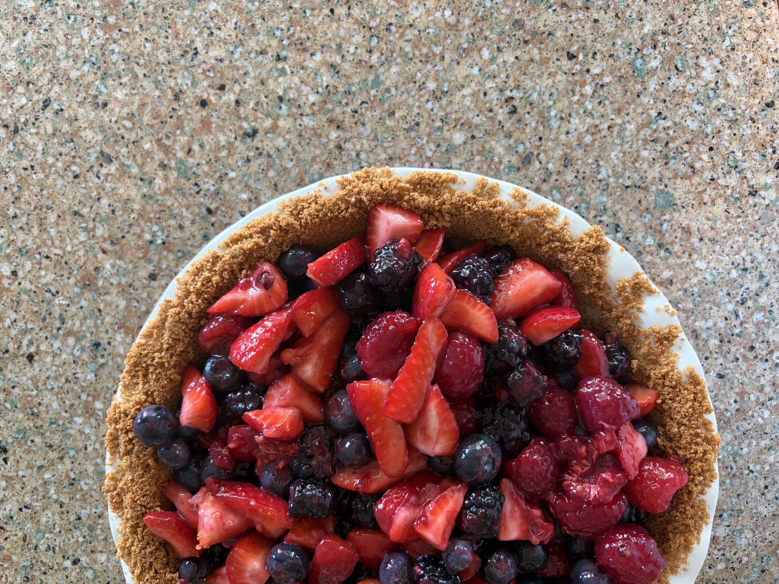 Half of a mixed berry pie sitting on the counter with a graham cracker crust. 