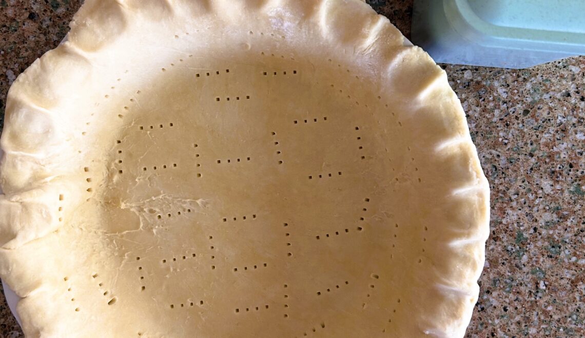 Single pie dough in pie plate on a counter with pie weights box in top right corner