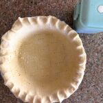 Single pie dough in pie plate on a counter with pie weights box in top right corner