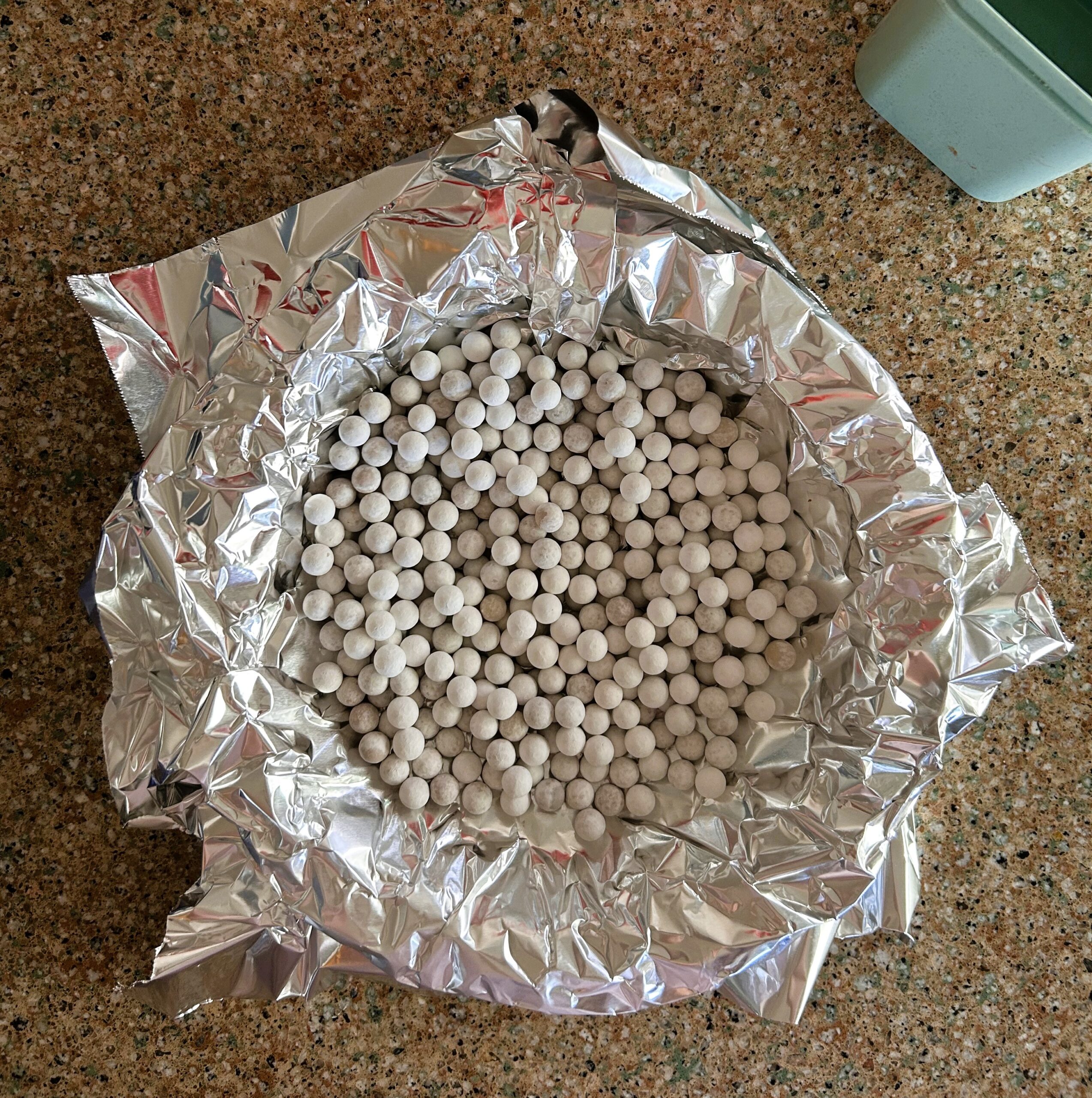 Pie dough covered in foil with pie weights in the center; pie plate is sitting on a granite counter.