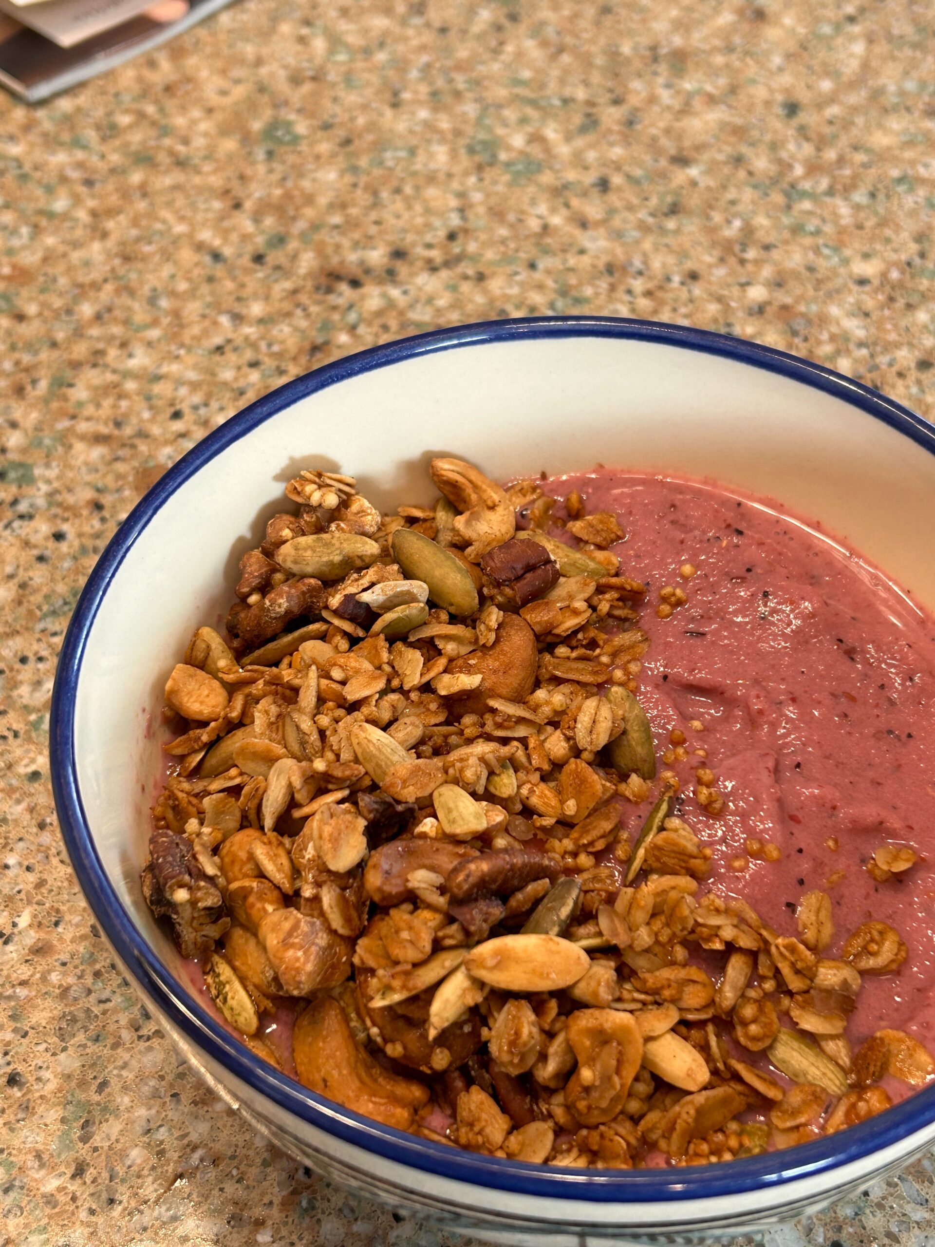 bowl filled with berry smoothie cover with granola that includes oats, puffed quinoa, 5 different types of nuts, and maple syrup.