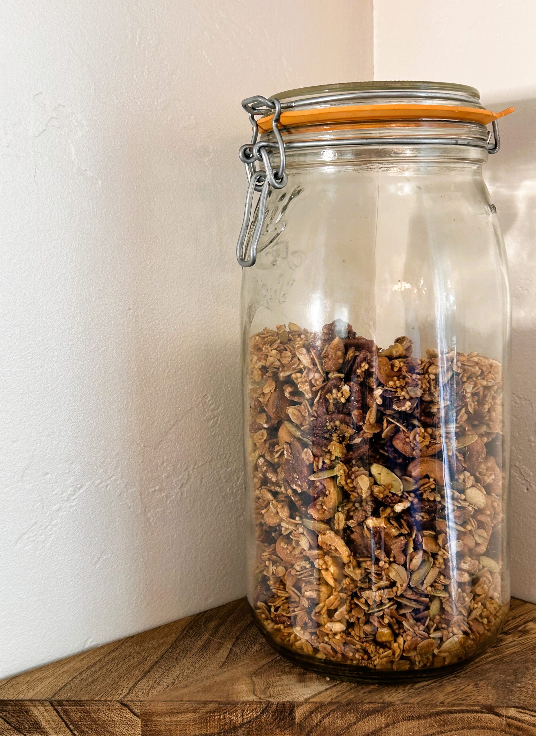 Homemade granola in a large mason jar on a wooden shelf.