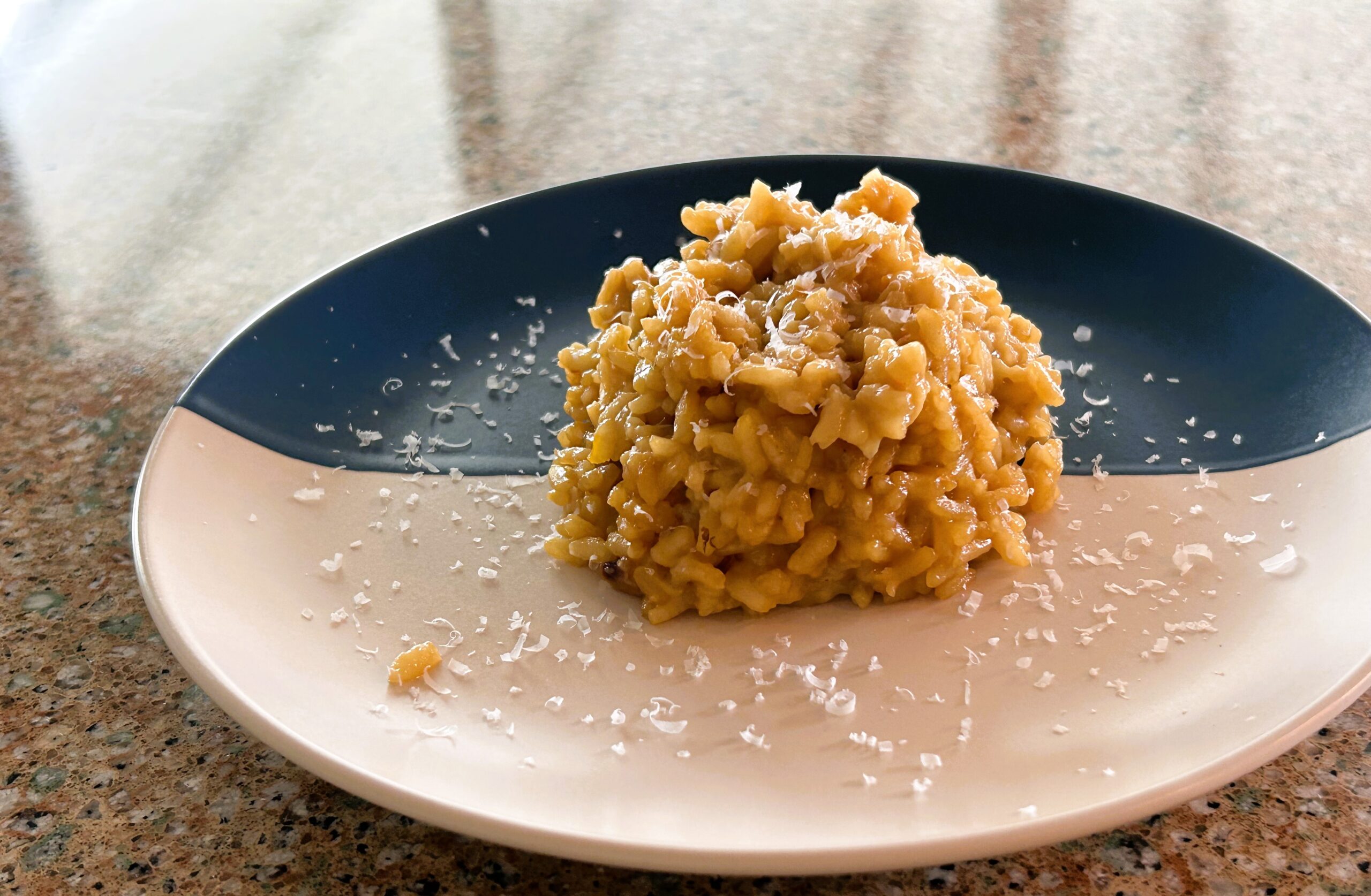 Saffron risotto positioned on a blue/white plate dusted with parmesan.