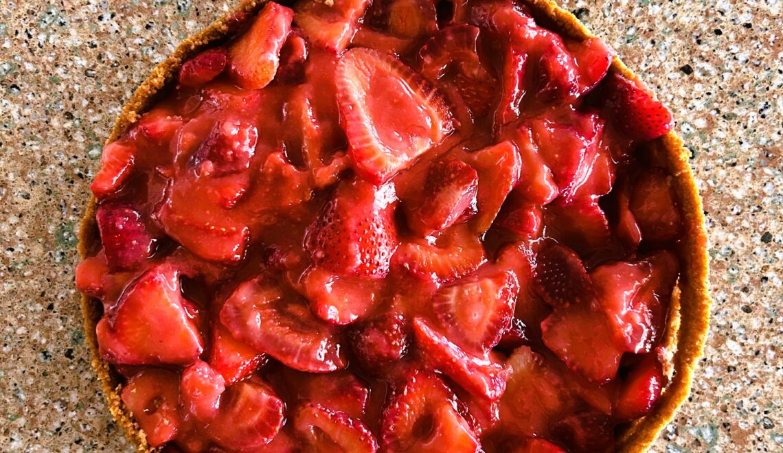fresh strawberry pie in graham cracker crust sitting on a granite counter.