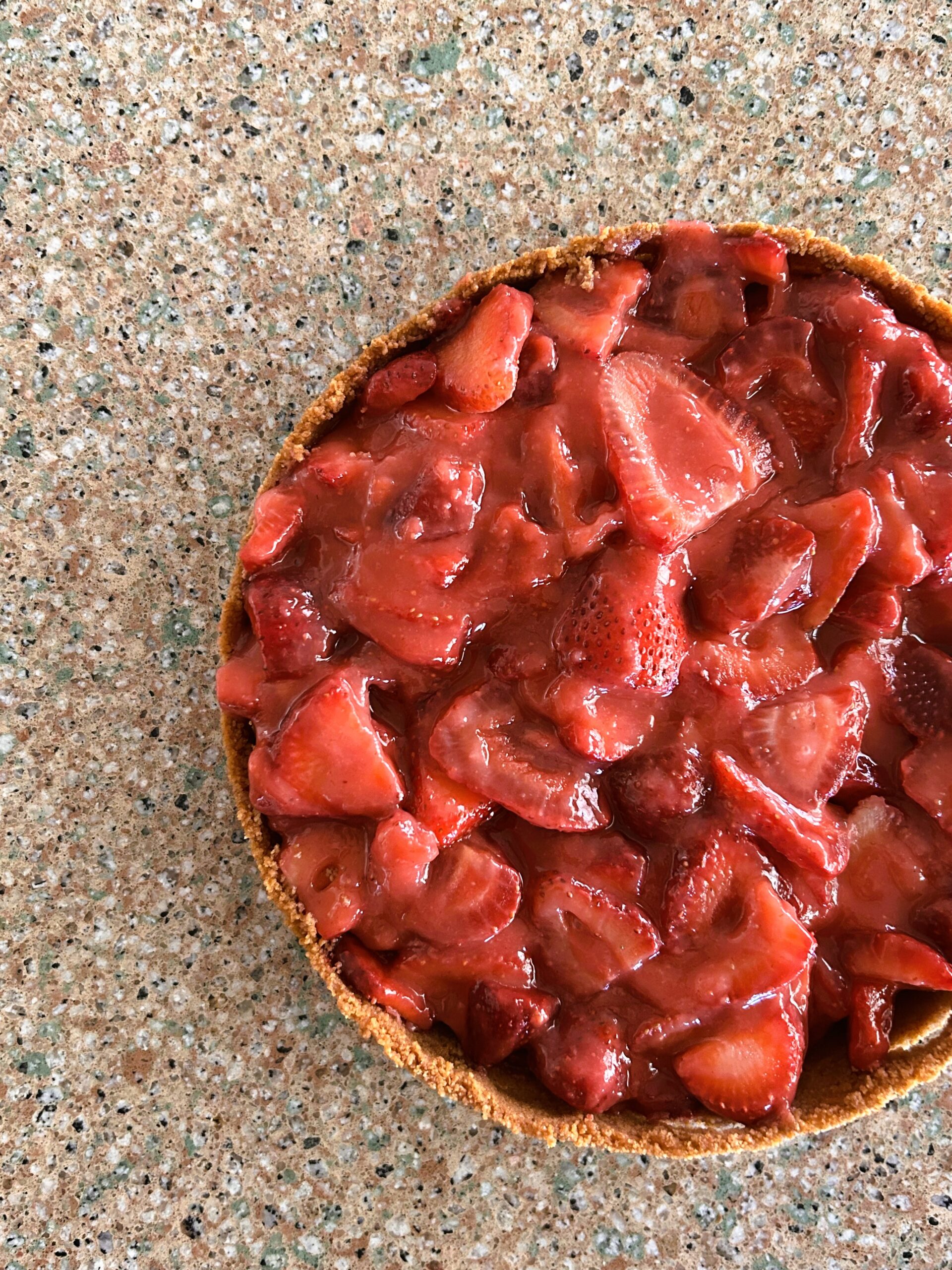 fresh strawberry pie in graham cracker crust sitting on a granite counter.