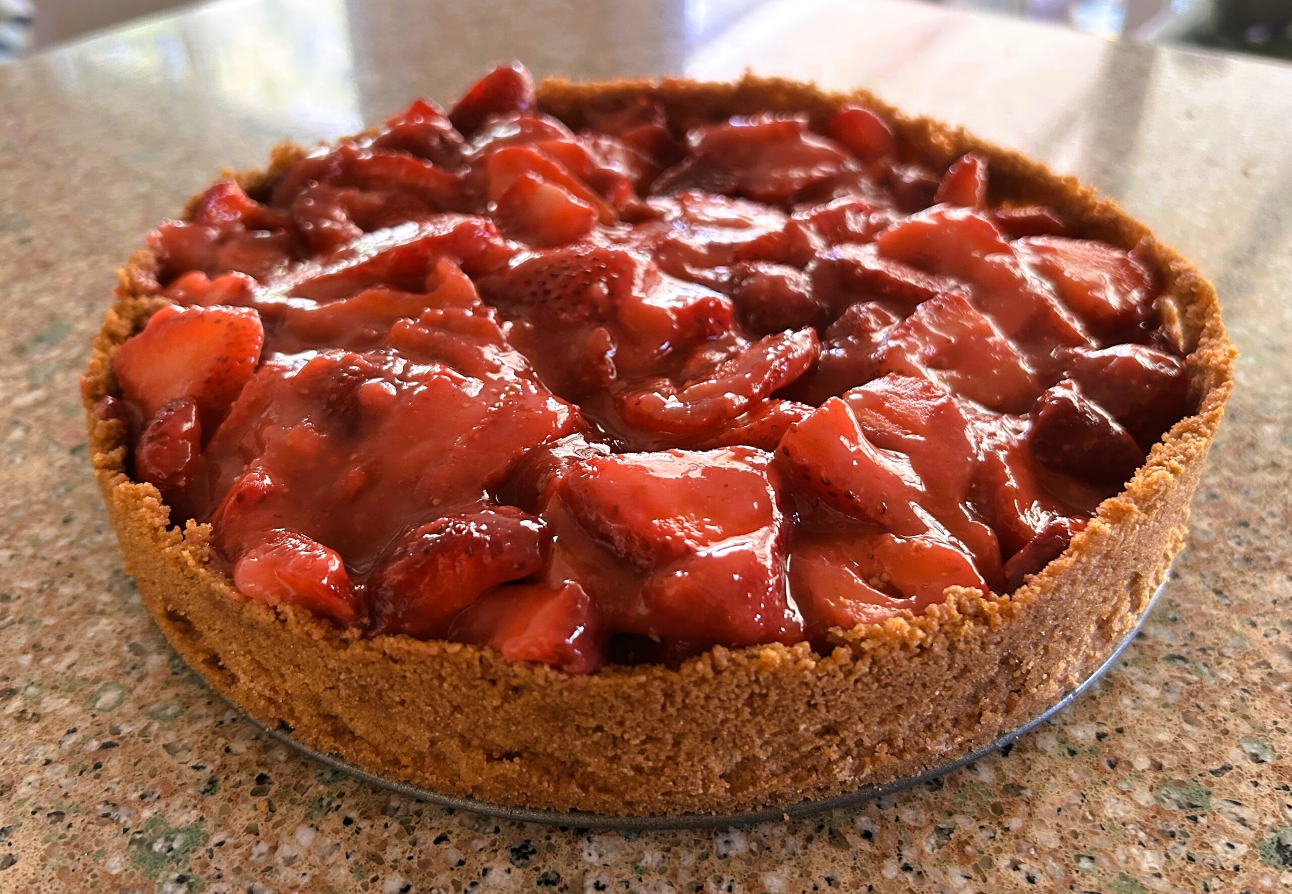 fresh strawberry pie in graham cracker crust sitting on a granite counter.