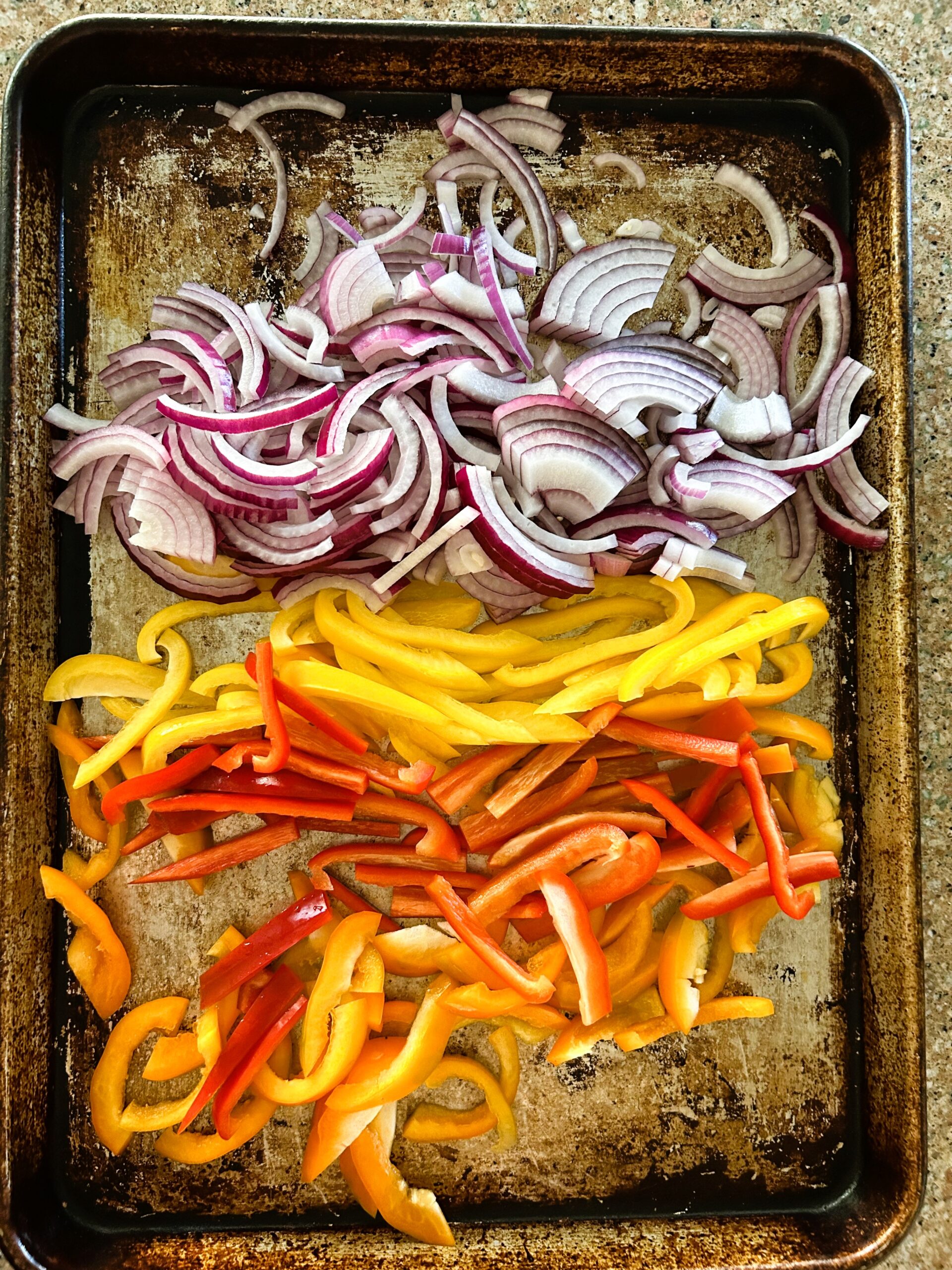 Julienned red onion, yellow, and red bell pepper on a sheet tray